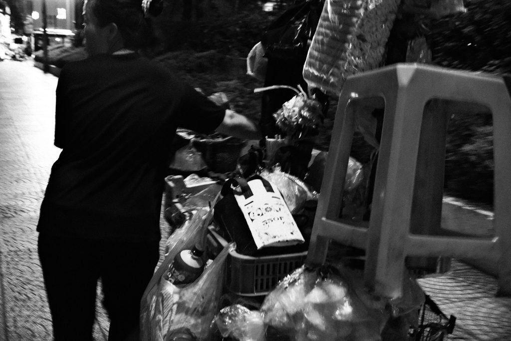 Vendeur ambulant poussant son vélo chargé de tabourets en plastique sur le trottoir