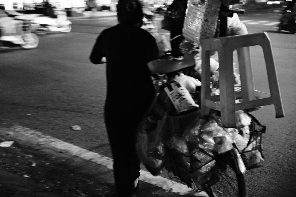 Vendeur ambulant traversant la rue avec un vélo chargé de tabourets et de marchandises