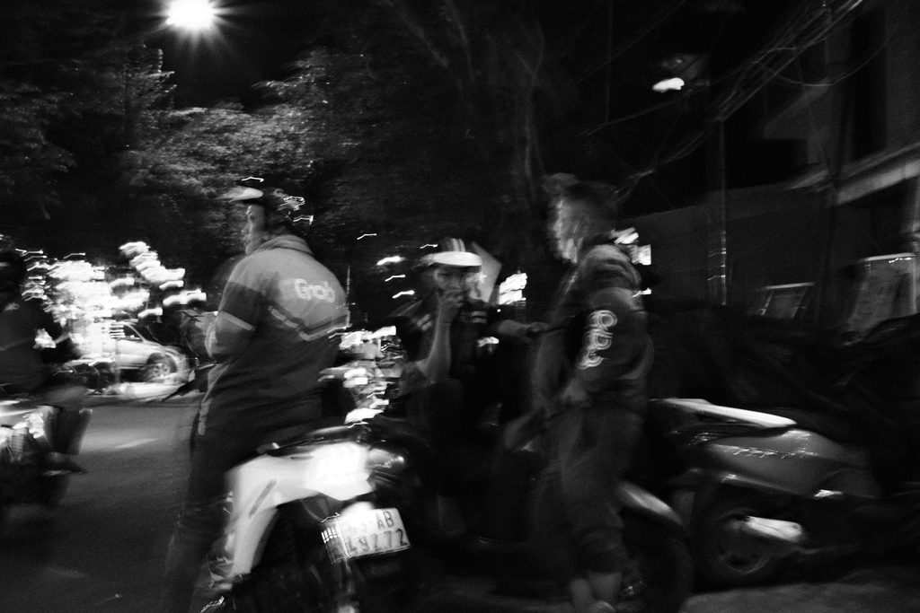 Scooters et passants dans une rue sous un lampadaire, la nuit