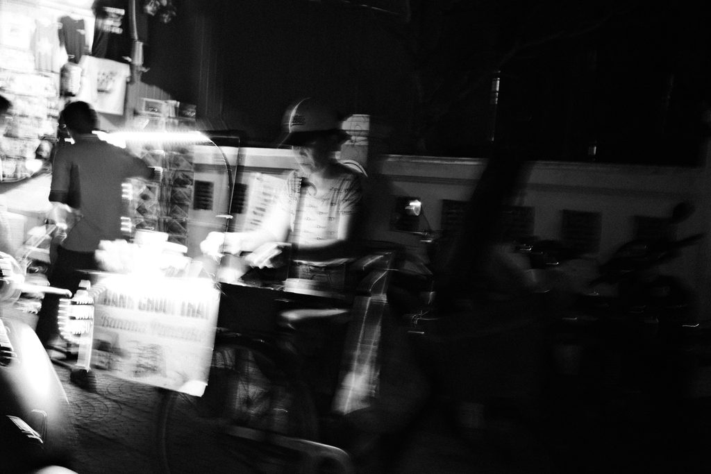 Chariot de vendeur de rue éclairé, entouré de silhouettes dans la nuit