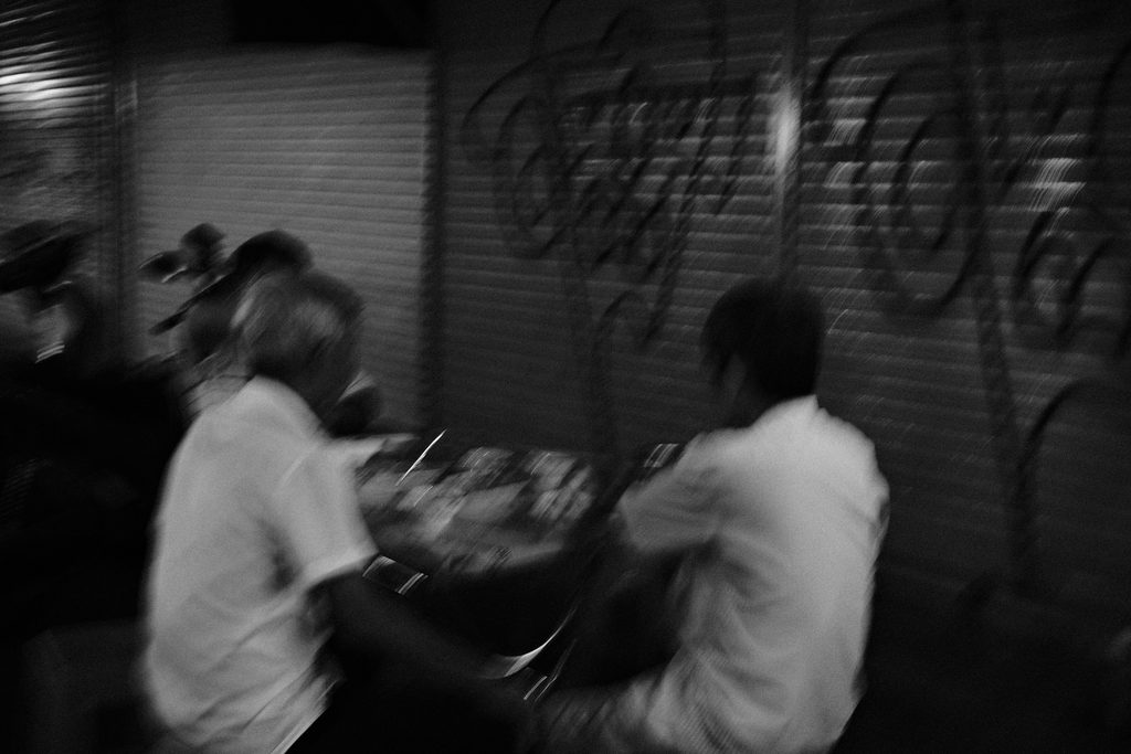 Deux hommes penchés sur leur repas, flous, devant un rideau de fer tagué