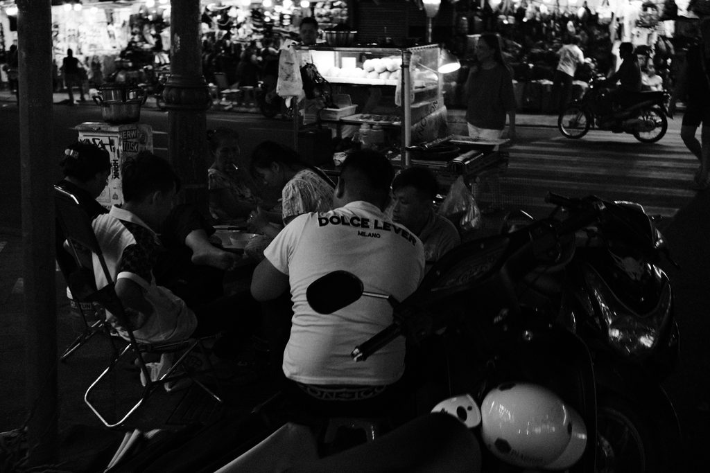 Convives de dos parmi les motos garées, dans une rue animée le soir