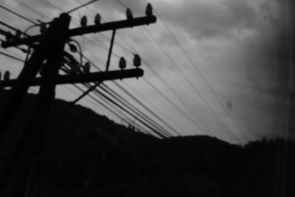 Poteau électrique et câbles en contre-jour sur un ciel chargé