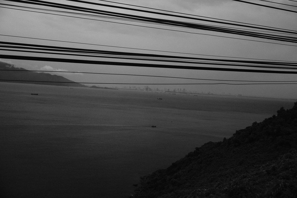 Baie et collines sous un ciel gris, barrées de câbles électriques, depuis le train au Vietnam