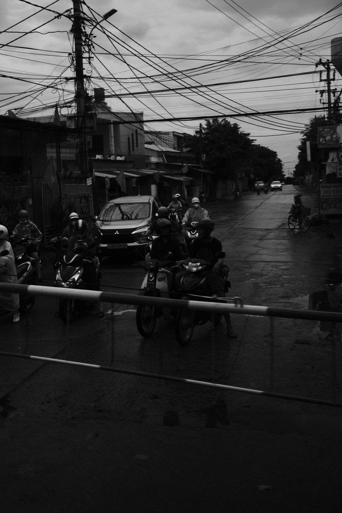 Motos et voitures à l'arrêt devant la barrière d'un passage à niveau, en ville