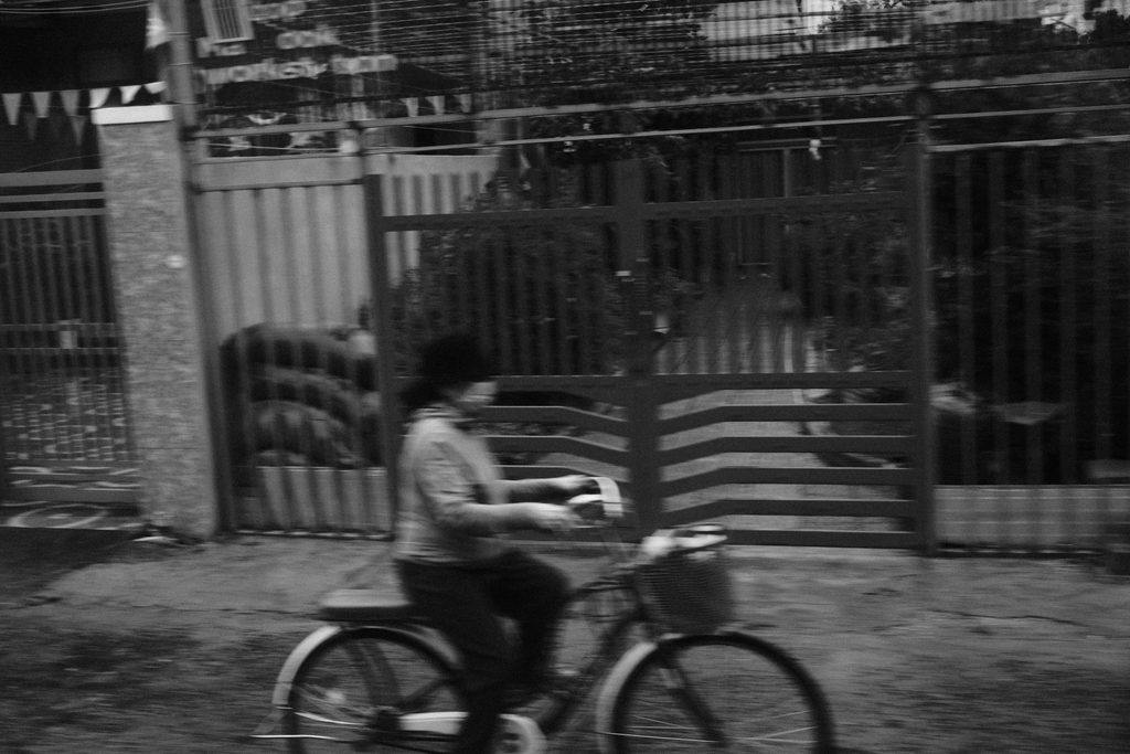 Une femme à vélo devant un portail, saisie depuis le train