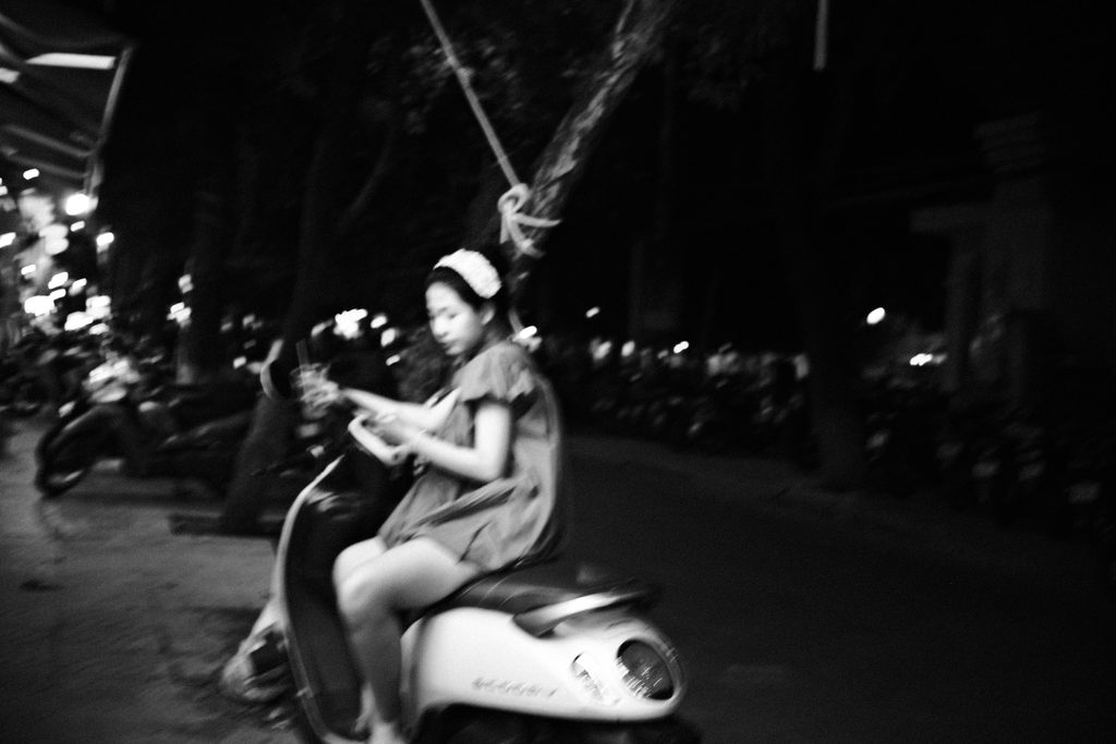 Jeune fille à scooter, téléphone en main, dans une rue sombre