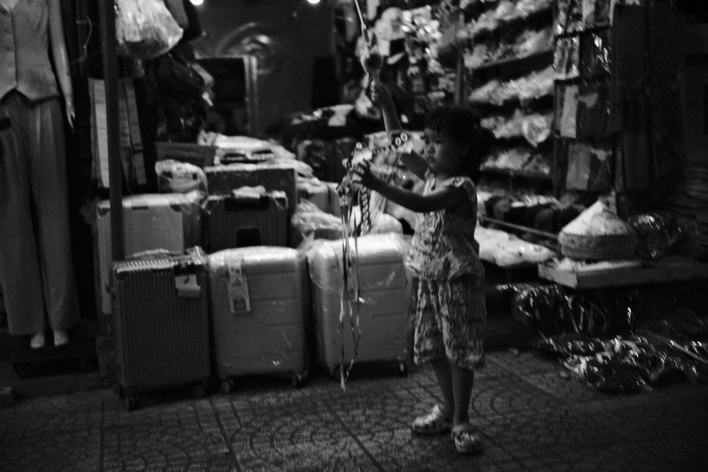 Un enfant debout devant les valises d'une boutique, absorbé par un objet entre ses mains
