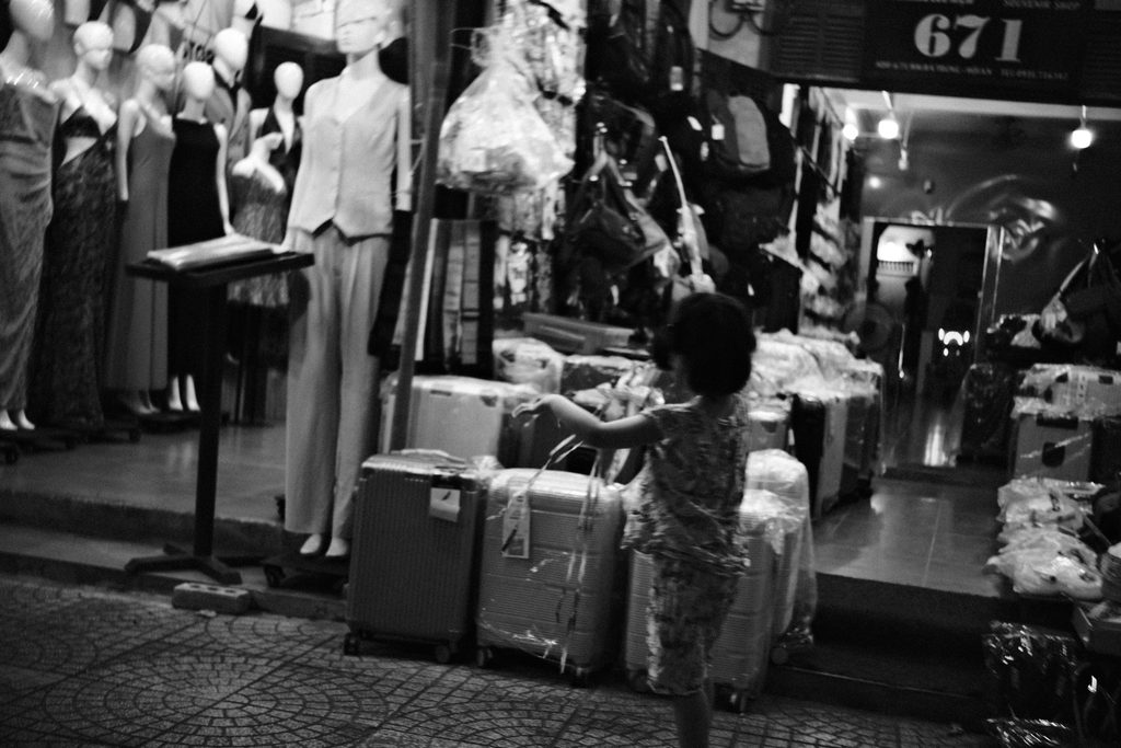 Un enfant lève les bras devant une vitrine de mannequins et de valises