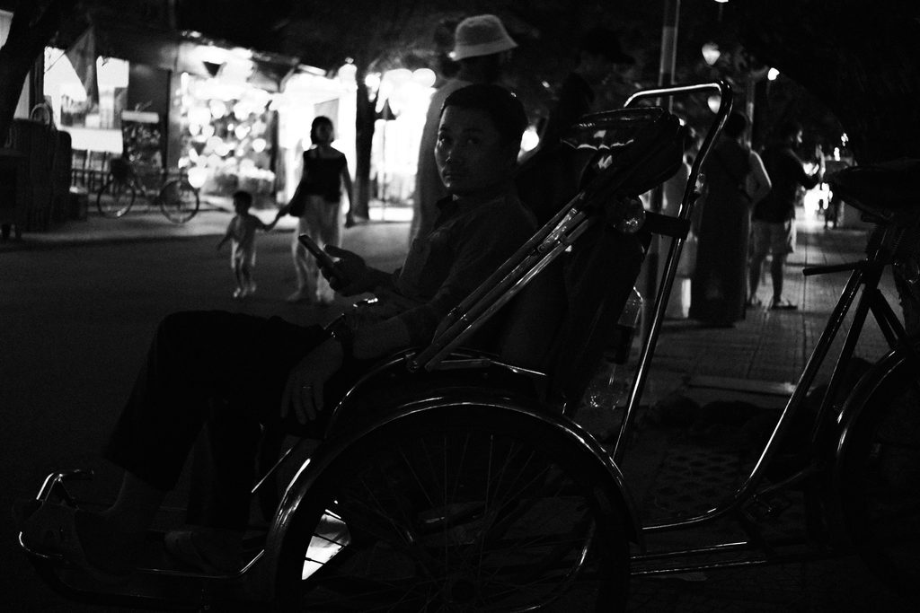 Silhouettes de cyclo-pousses et de passants sous un auvent, à contre-jour
