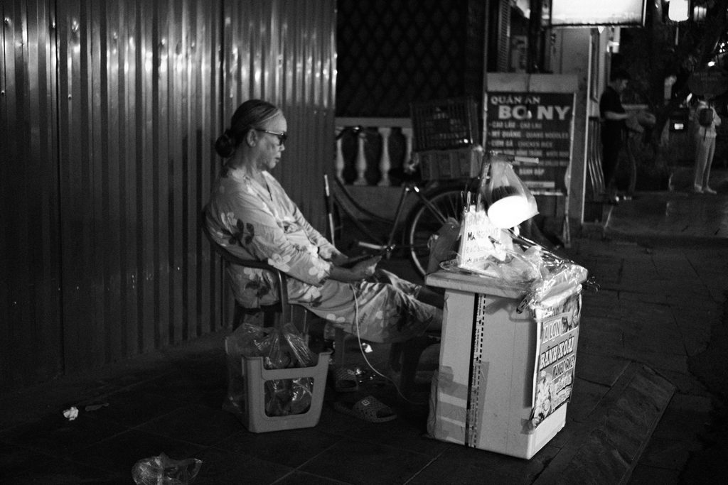 Vendeuse âgée assise près de son étal éclairé sur le trottoir