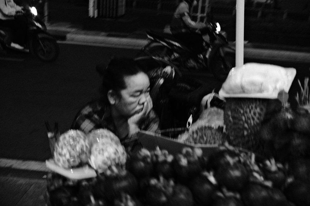 Vendeuse accoudée derrière ses fruits et légumes, sur le trottoir