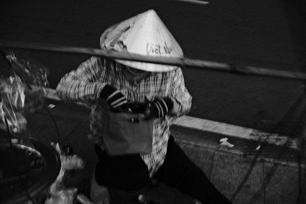 Vendeuse au chapeau conique assise au bord du trottoir