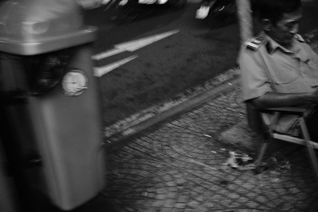 Homme assis sur le trottoir à côté d'une poubelle, scooters flous en arrière-plan