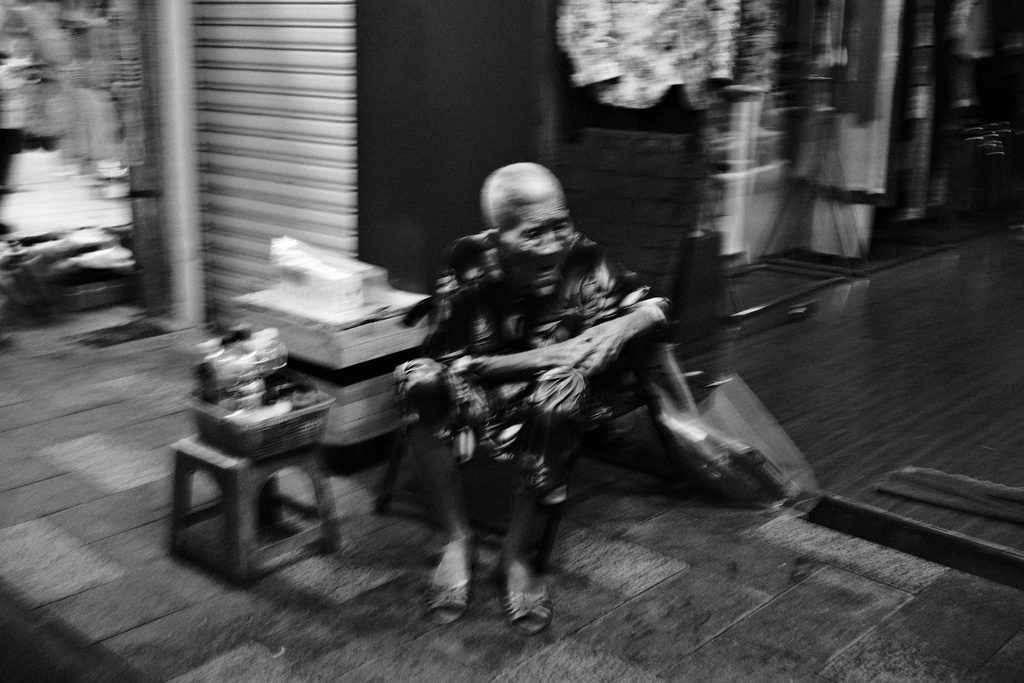 Femme âgée assise sur le trottoir devant un rideau de fer, à Hô Chi Minh-Ville