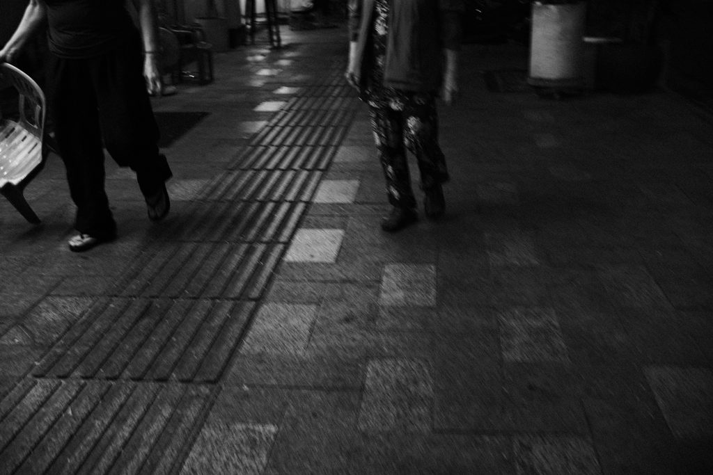 Jambes de passants sur un trottoir sombre, à Hô Chi Minh-Ville