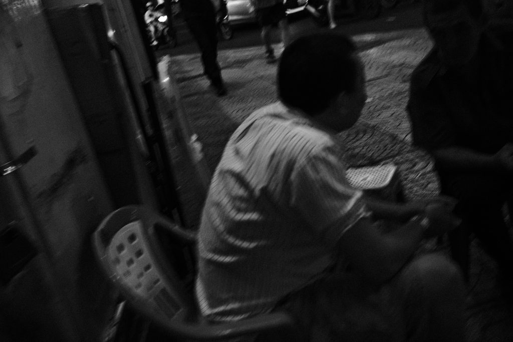 Homme de dos assis sur une chaise en plastique, dans une ruelle sombre
