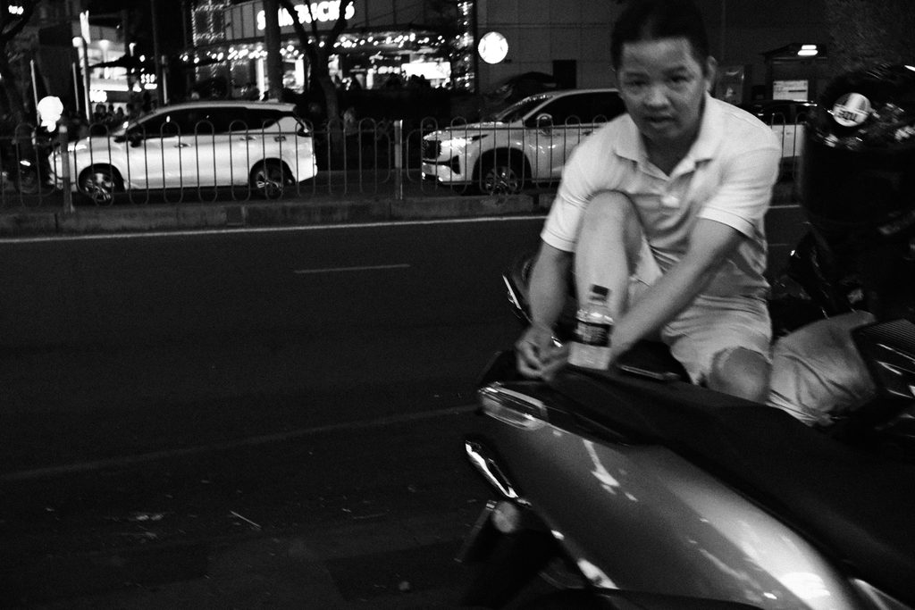 Jeune homme assis sur un scooter au bord d'une avenue, la nuit