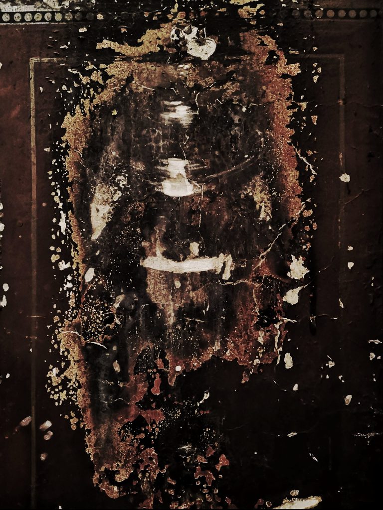 Mur d’église noirci par la fumée des bougies votives, peinture écaillée, traces de couleur : des années de prières déposées en suie.